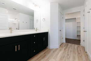 Full bath with a walk in closet, double vanity, a shower stall, and light wood-type flooring