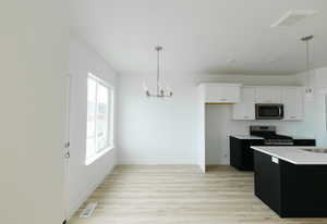 Kitchen featuring dark cabinets, white cabinetry, a chandelier, decorative light fixtures, and light wood finished floors