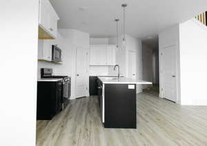 Kitchen with appliances with stainless steel finishes, a center island with sink, white cabinets, dark cabinetry, and decorative light fixtures