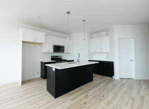 Kitchen featuring dark cabinets, white cabinetry, a kitchen island with sink, and stainless steel appliances