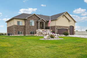 View of front facade with stucco siding, a front lawn, and stone siding