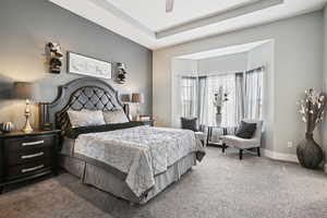 Bedroom with carpet flooring, a tray ceiling, and a ceiling fan
