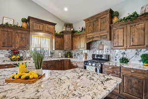 Kitchen with stainless steel gas range, light stone countertops, decorative backsplash, vaulted ceiling, and recessed lighting