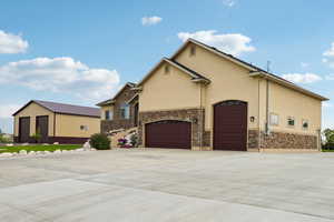 View of front facade featuring stucco siding, driveway, stone siding, and an attached garage
