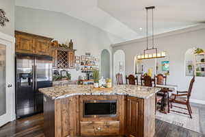 Kitchen with appliances with stainless steel finishes, light stone countertops, dark wood-type flooring, a kitchen island, and lofted ceiling