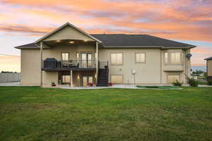 Back of house at dusk featuring stairway, a patio area, stucco siding, and a lawn
