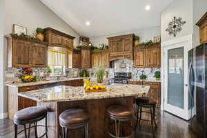 Kitchen with dark wood-type flooring, a breakfast bar area, stainless steel appliances, light stone counters, and lofted ceiling