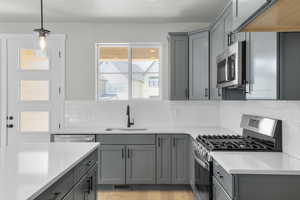 Kitchen featuring gray cabinets, stainless steel appliances, decorative light fixtures, light wood finished floors, and decorative backsplash