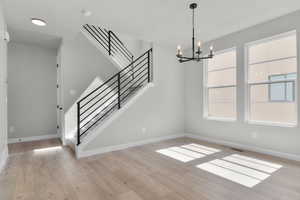 Unfurnished dining area with a chandelier, light wood-style floors, and stairs