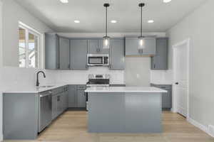Kitchen with a center island, decorative light fixtures, light stone countertops, stainless steel appliances, and light wood-type flooring