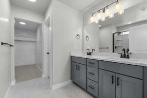 Full bathroom featuring a spacious closet, double vanity, and light marble finish floors