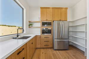 Kitchen with stainless steel appliances, open shelves, brown cabinetry, and light wood finished floors