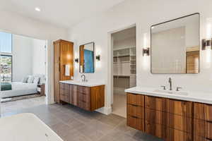 Full bathroom featuring two vanities, light tile patterned floors, recessed lighting, a freestanding bath, and connected bathroom