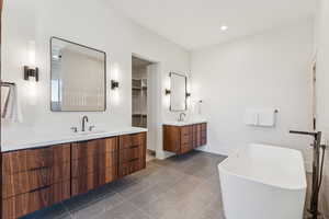 Full bathroom featuring two vanities, a freestanding tub, dark tile patterned flooring, and recessed lighting