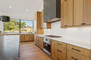Kitchen featuring wall chimney exhaust hood, hanging light fixtures, light wood-style floors, recessed lighting, and stainless steel appliances