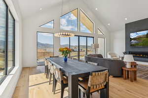 Dining space featuring high vaulted ceiling, light wood-style floors, a large fireplace, recessed lighting, and a chandelier