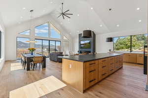 Kitchen featuring high vaulted ceiling, modern cabinets, decorative light fixtures, a large island, and light wood-type flooring