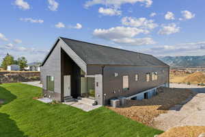 Back of house with entry steps, a shingled roof, a mountain view, and a lawn