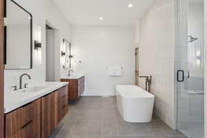 Bathroom featuring a shower stall, two vanities, dark tile patterned floors, a soaking tub, and recessed lighting