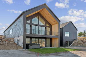 Rear view of property featuring a hot tub, a balcony, and a patio area