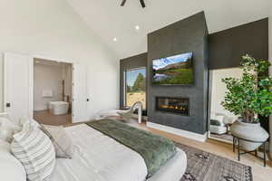 Bedroom with high vaulted ceiling, wood finished floors, recessed lighting, a fireplace, and connected bathroom