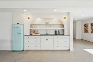 Kitchen featuring freestanding refrigerator, open shelves, white cabinetry, recessed lighting, and dark aggregate flooring