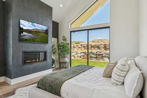Bedroom with wood finished floors, a large fireplace, recessed lighting, access to outside, and a towering ceiling