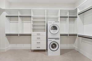 Walk in closet featuring estacked washer and dryer and light colored carpet
