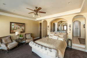 Carpeted bedroom featuring a raised ceiling, a ceiling fan, and arched walkways
