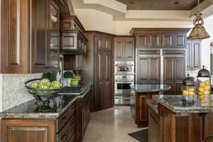 Kitchen featuring decorative backsplash, decorative light fixtures, dark stone counters, a tray ceiling, and a center island