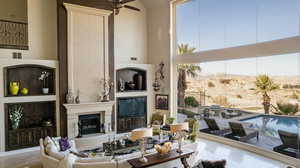 Living room featuring a high ceiling, a large fireplace, ceiling fan, and view of desert landscape