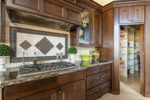 Kitchen featuring custom exhaust hood, dark stone counters, dark brown cabinets, and stainless steel gas stovetop