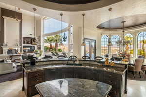 Kitchen featuring dark brown cabinets, open floor plan, a tray ceiling, decorative light fixtures, and a center island with sink