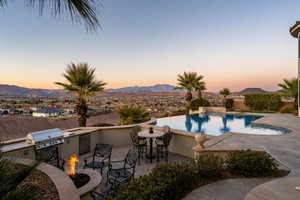 Pool at dusk with an outdoor fire pit, grilling area, an outdoor pool, and a mountain view