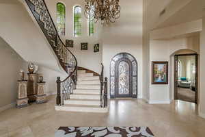 Foyer with arched walkways, healthy amount of natural light, a high ceiling, a chandelier, and stairs