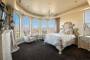 Bedroom featuring a tray ceiling, a chandelier, and dark colored carpet