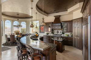 Kitchen with a raised ceiling, glass insert cabinets, dark stone counters, decorative light fixtures, and a kitchen bar