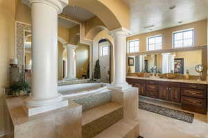 Bathroom with vanity, a bath, light tile patterned floors, a textured ceiling, and ornate columns