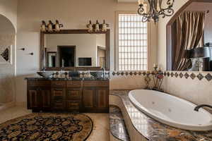 Full bath featuring a tub with jets, double vanity, a chandelier, and light tile patterned floors