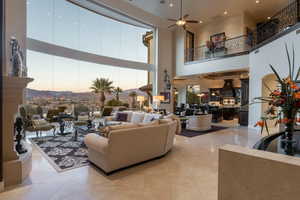 Living area with a towering ceiling, a ceiling fan, light tile patterned floors, and floor to ceiling windows