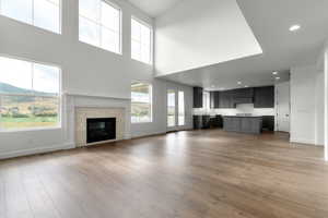Unfurnished living room with dark wood-style floors, a tiled fireplace, a mountain view, recessed lighting, and a high ceiling
