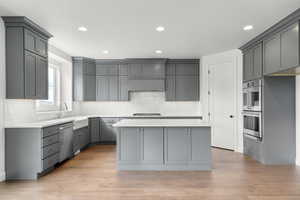 Kitchen with gray cabinetry, a kitchen island, recessed lighting, light wood-style flooring, and tasteful backsplash