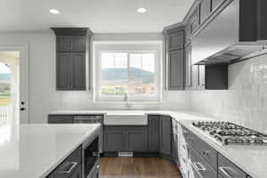 Kitchen with gray cabinetry, custom range hood, stainless steel appliances, dark wood-style flooring, and light stone counters