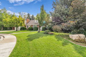 View of front of property with a front yard, brick siding, a chimney, and concrete driveway