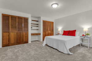 Bedroom featuring a textured ceiling, multiple closets, and light carpet