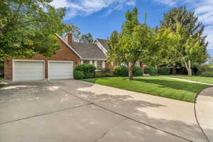 View of front of property with brick siding, a front lawn, concrete driveway, an attached garage, and a chimney