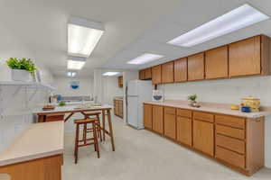 Kitchen featuring light floors, light countertops, brown cabinetry, freestanding refrigerator, and open shelves