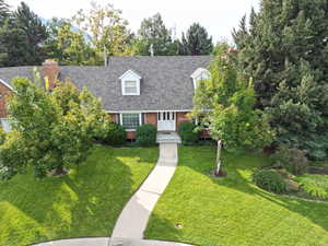 Cape cod-style house with a front yard, roof with shingles, brick siding, and view of scattered trees