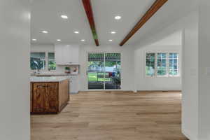 Kitchen featuring beamed ceiling, white cabinets, light stone counters, light wood-style floors, and decorative backsplash