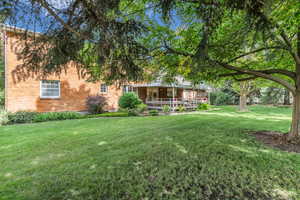 Rear view of property with brick siding, a porch, and a yard